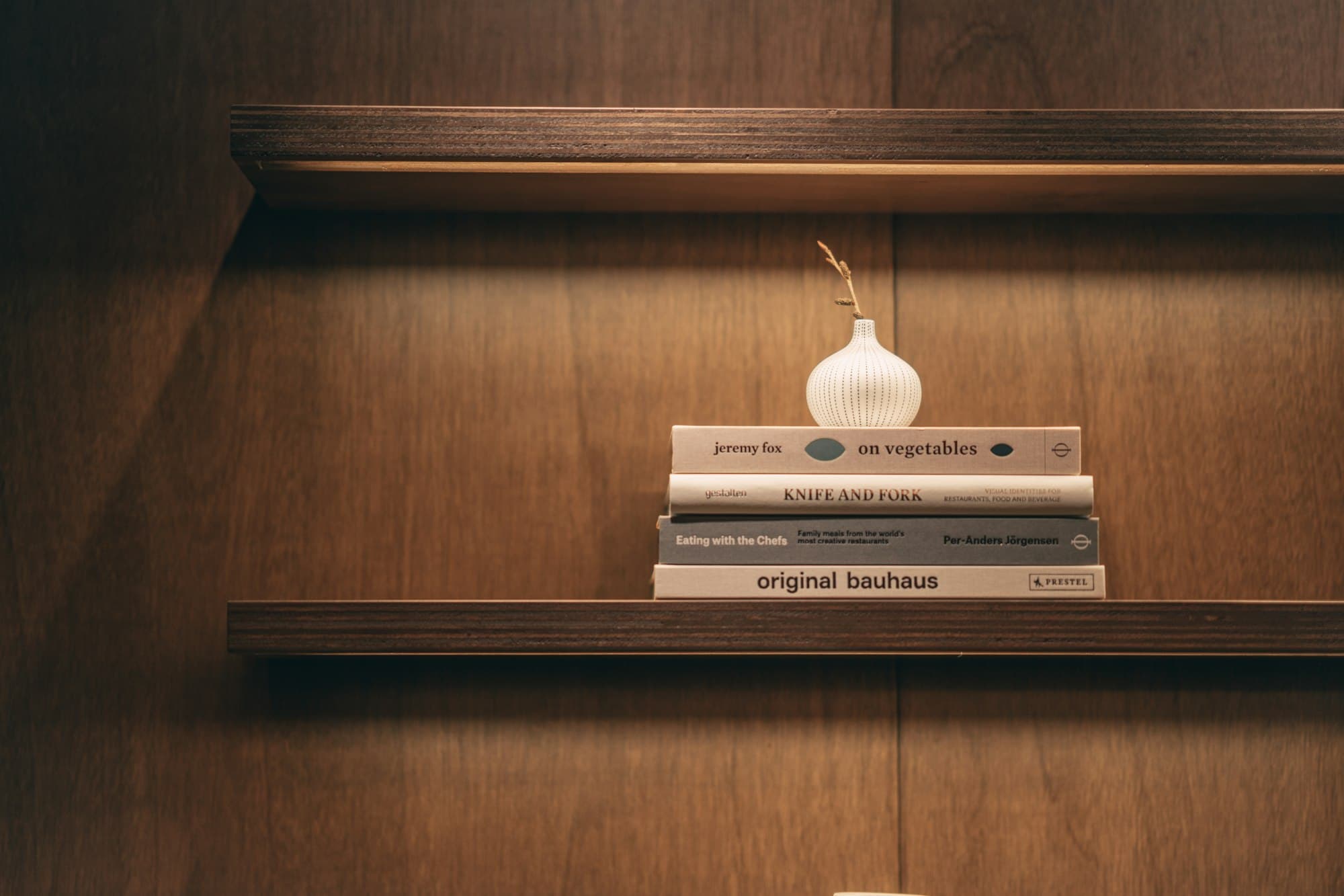 Holzregal an einer dunklen Holzwand mit Büchern und Vase
